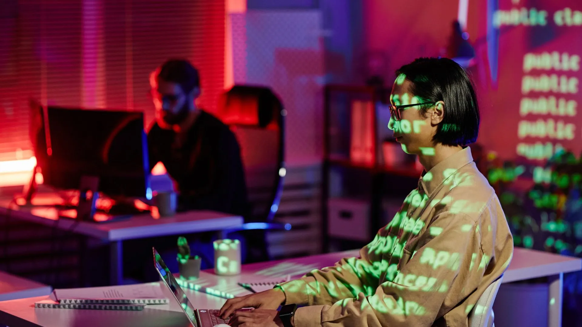 Senior engineer at a laptop with code projected across the room - the vibe coding workflow in motion, with AI generating code while the engineer reviews and shapes architecture